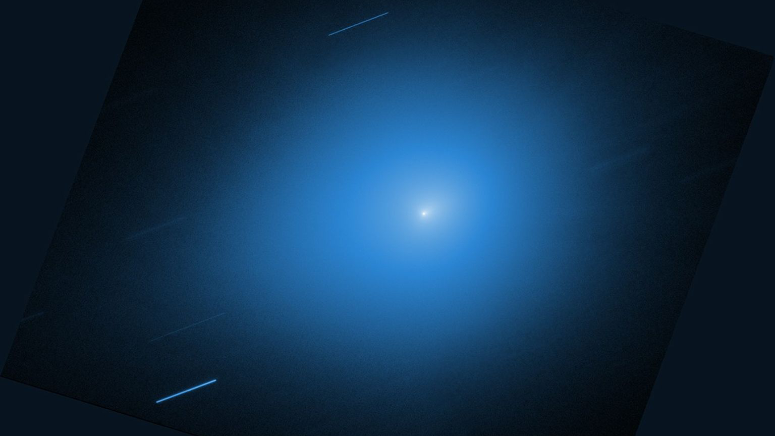 An image from NASA’s Hubble Space Telescope showing the interstellar comet 3I/ATLAS. The comet is a small white dot in the center of the image, with a light blue halo of light that takes up most of the image. Other stars are shown streaking across the image as diagonal blue-white lines.